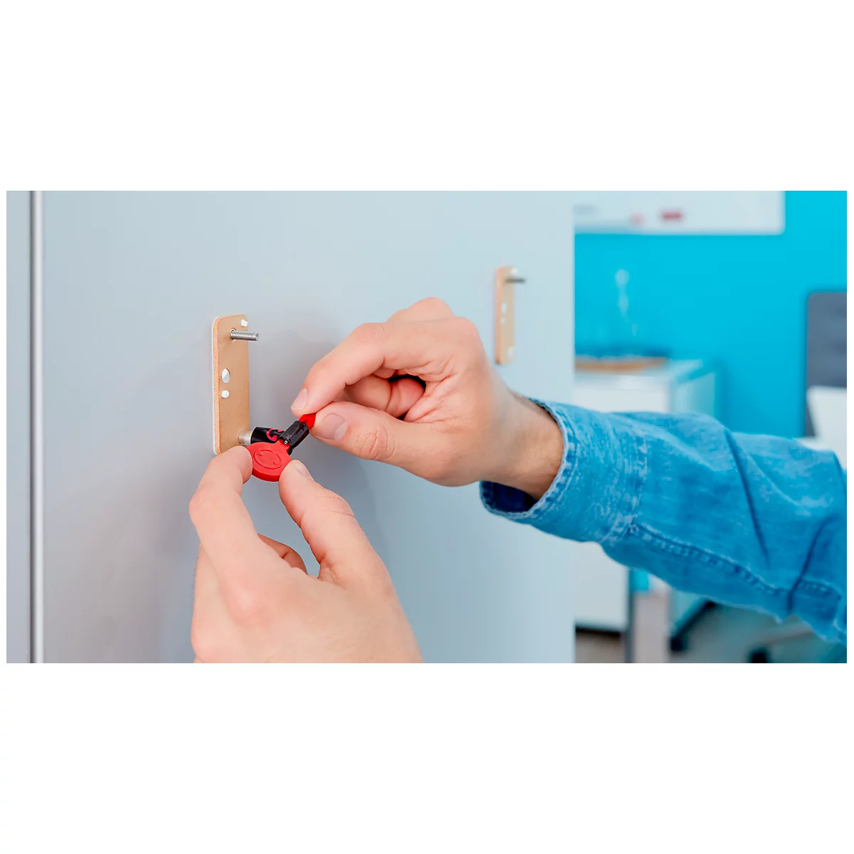 Hands hold a red key in front of a cabinet. The key is presumably for the cabinet.