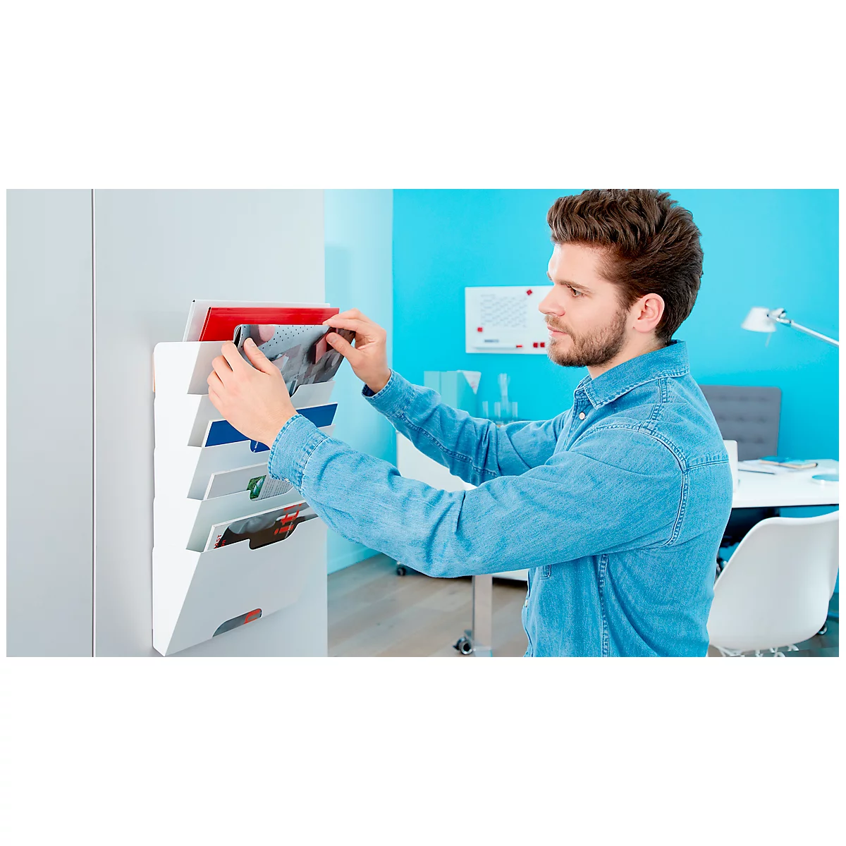 A man is putting a brochure into a white wall organizer.