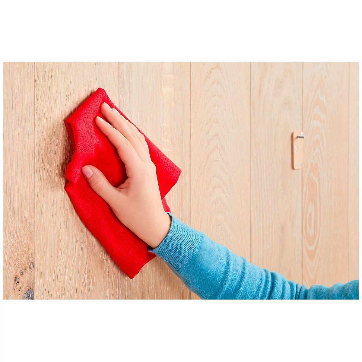 A hand wiping a wooden wall with a red cloth. A door handle can be seen in the background.