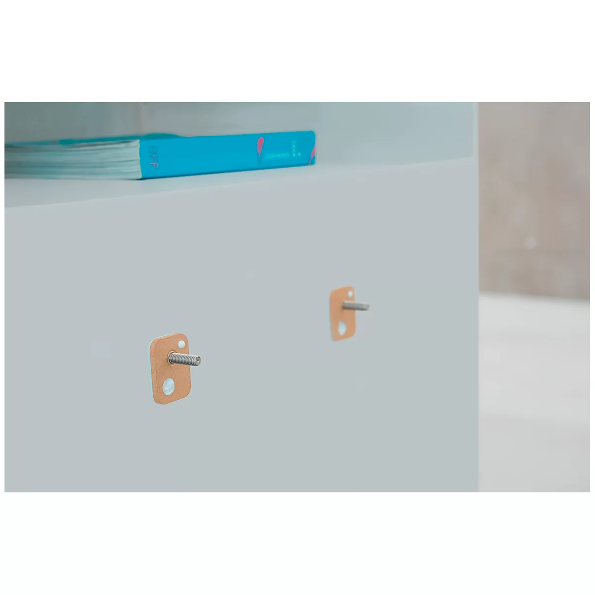 Close-up of a white dresser with two orange fittings and a book.