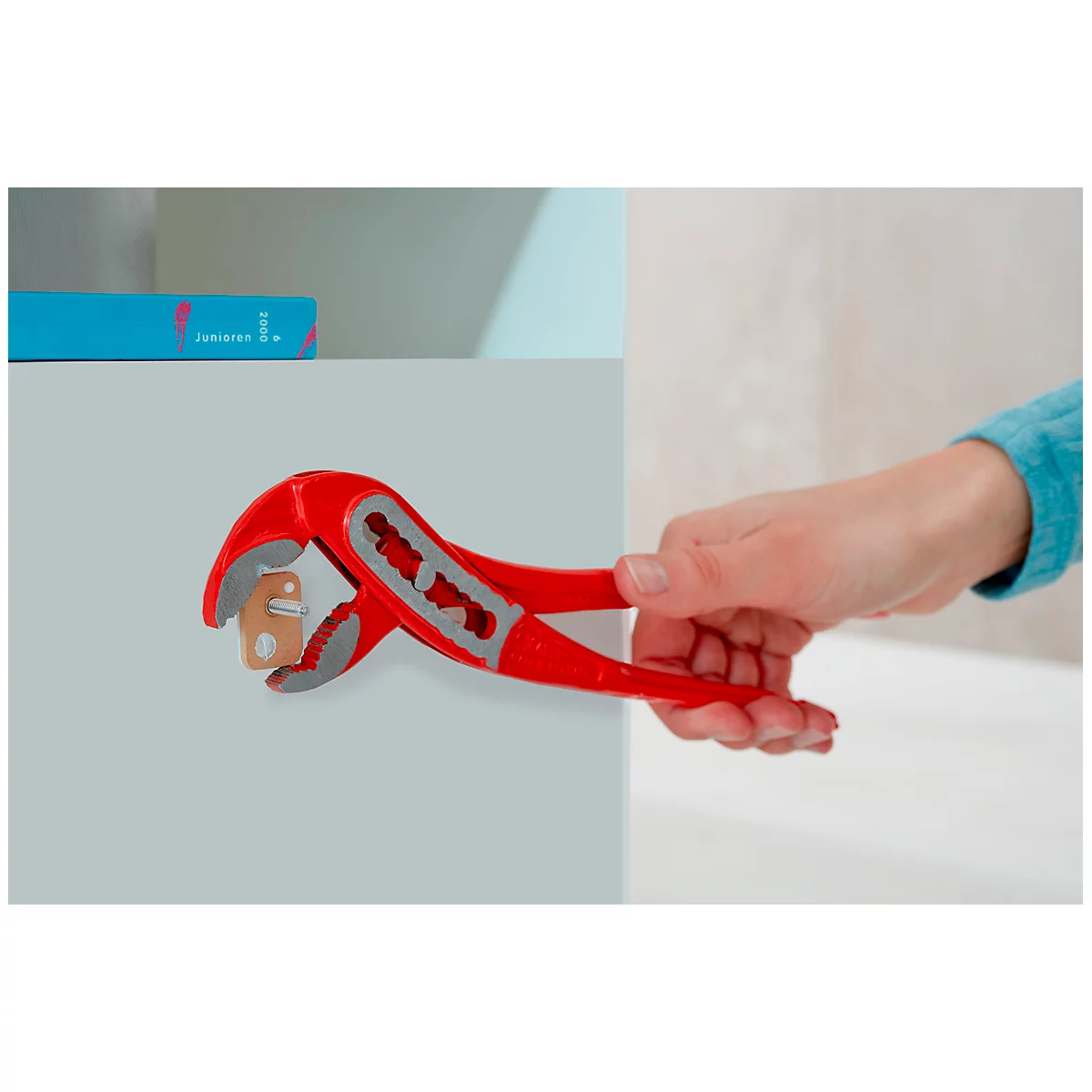 Red pliers hold a wooden cube. An arm with a blue sleeve holds the pliers.