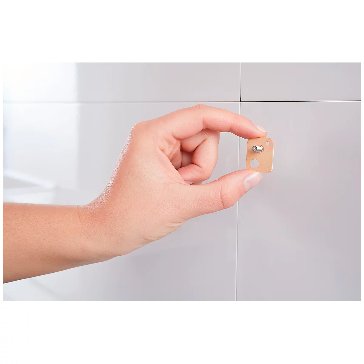 A hand holds a small, beige card with a silver pin against a white wall.