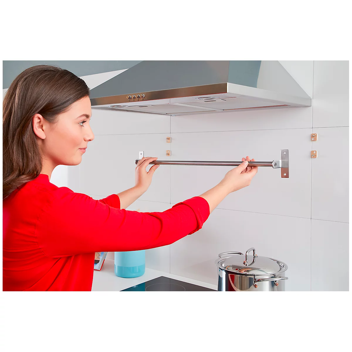 Woman installing a towel rack in the kitchen. She's wearing a red top. In the background, a hood and cooking utensils.