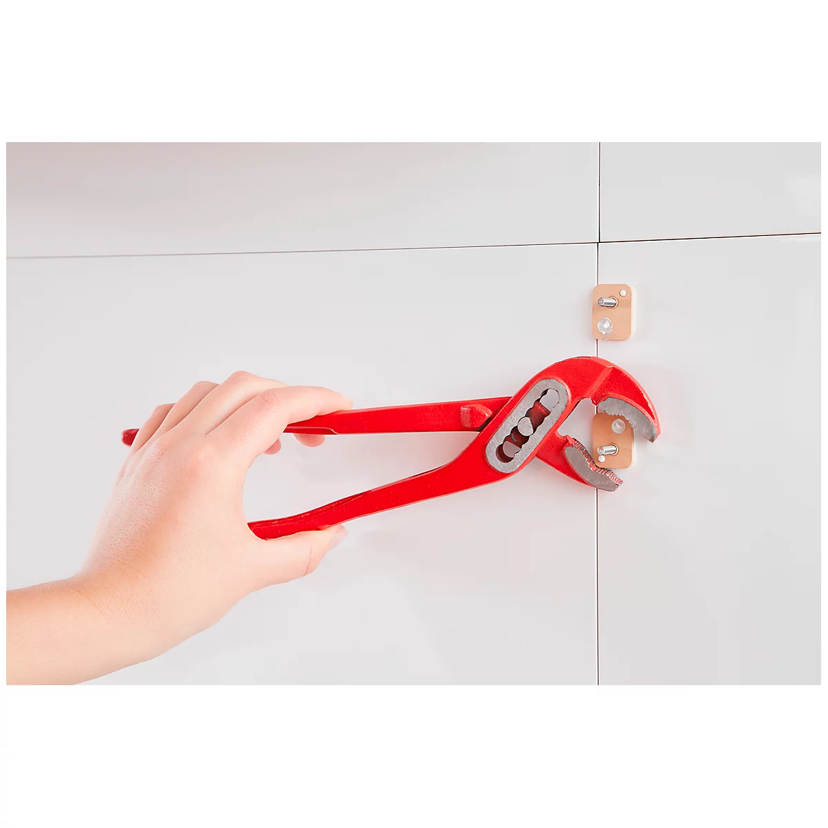 Hand holding red pliers working on a dowel on a white wall.