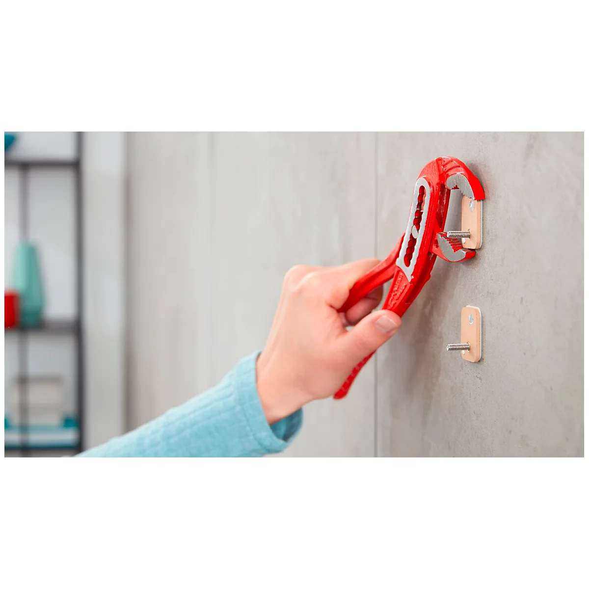 Person attaching red hook to wall. Tool is being used.