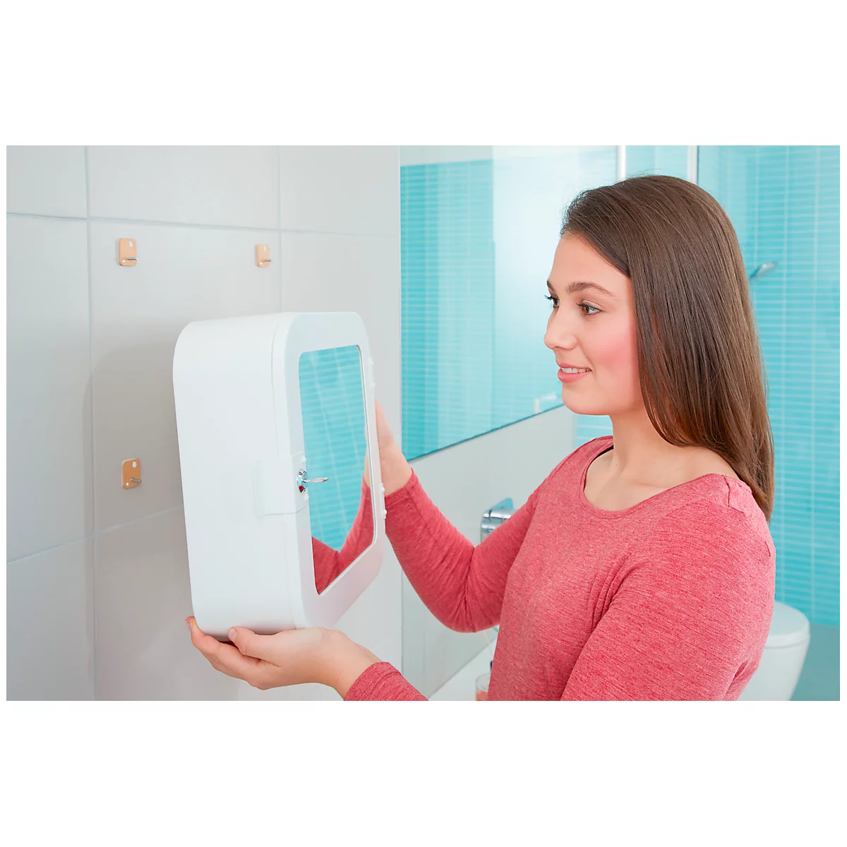 A young woman touches a white bathroom utensil. She smiles, with a sink and tiles in the background.