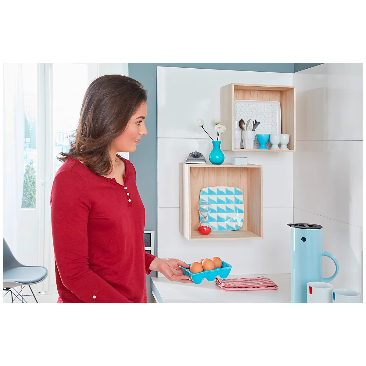 Woman in red shirt holding egg carton. Kitchen shelves with decor and utensils. Light blue water jug.