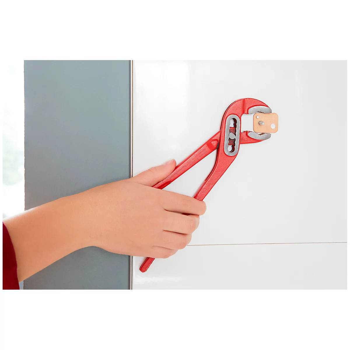 A red wrench holds a light rectangle against a white wall. An arm holds the wrench.