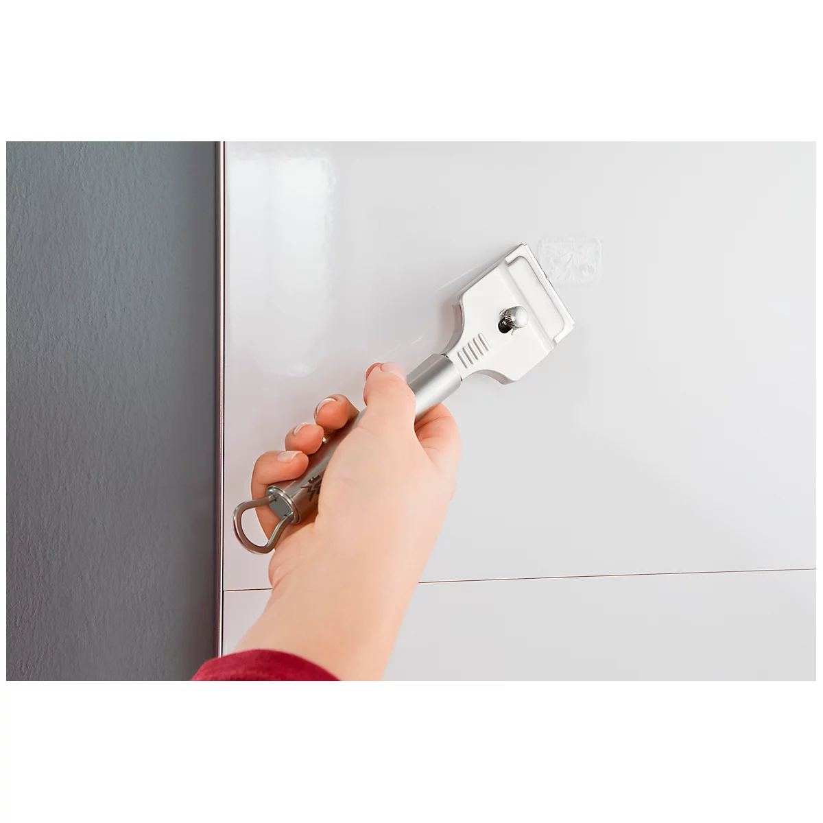 Person holding a metal scraper to remove residue from a white surface.