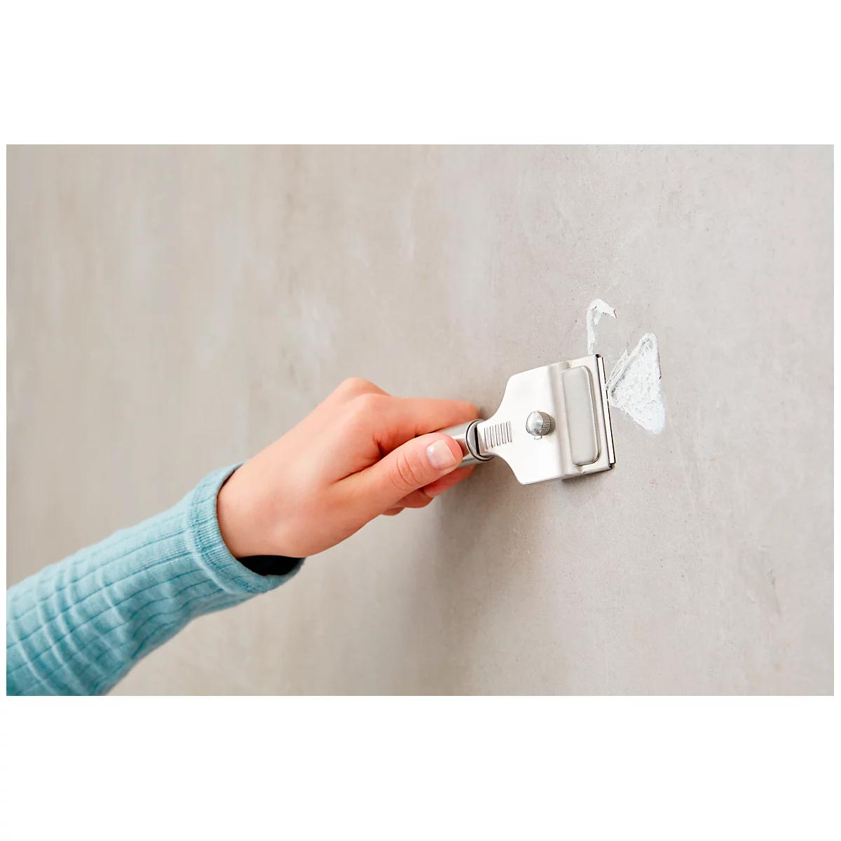 Close-up of a hand using a scraper on a wall to remove a small amount of putty.