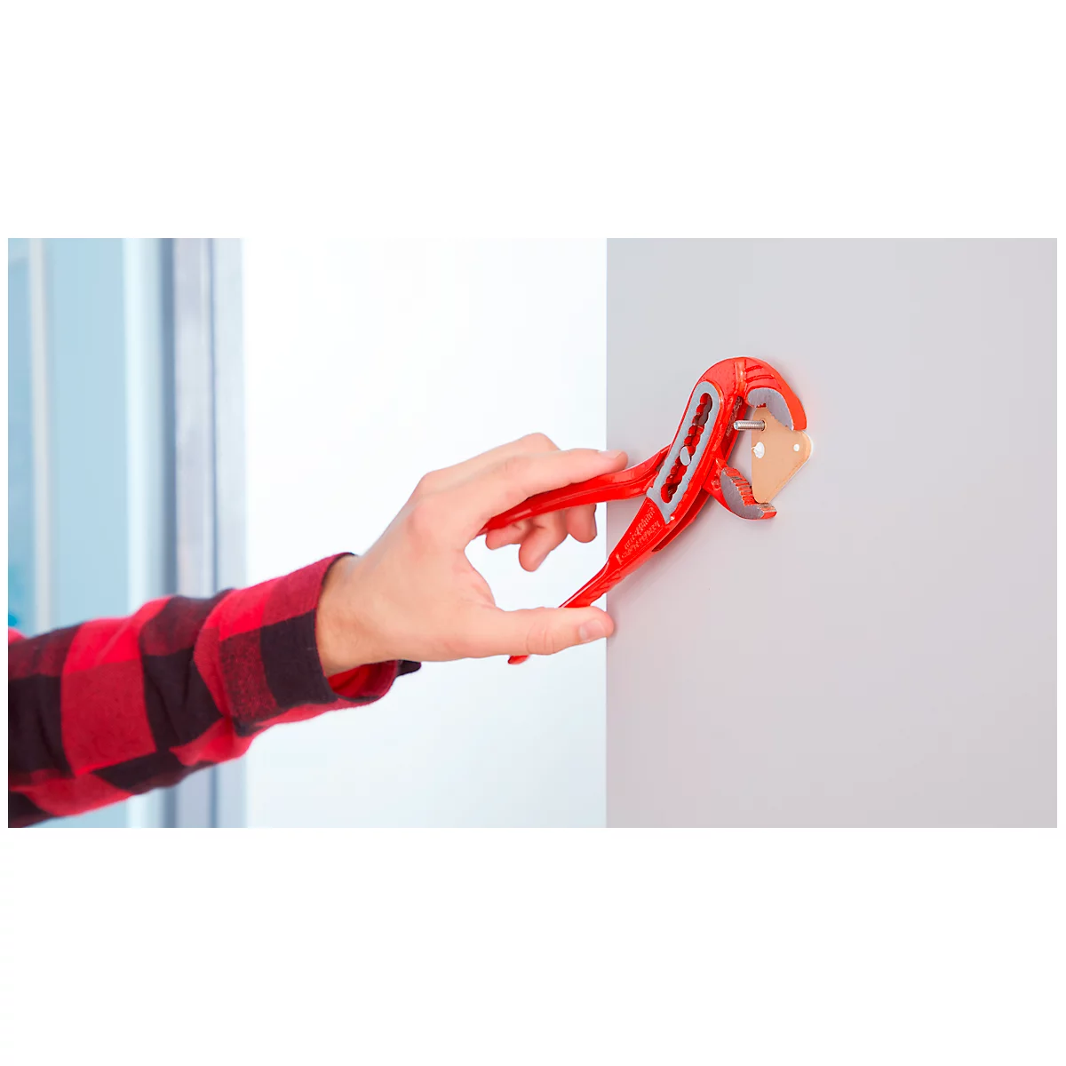 A person's hand holds a red electrical outlet. A red, pliers-like tool is being used.