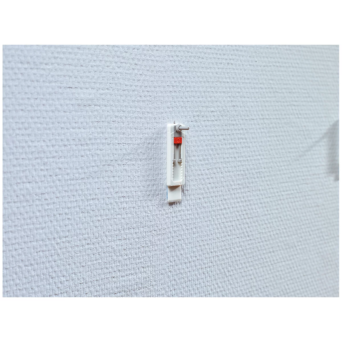 A white picture hook with red detail on a white wall.