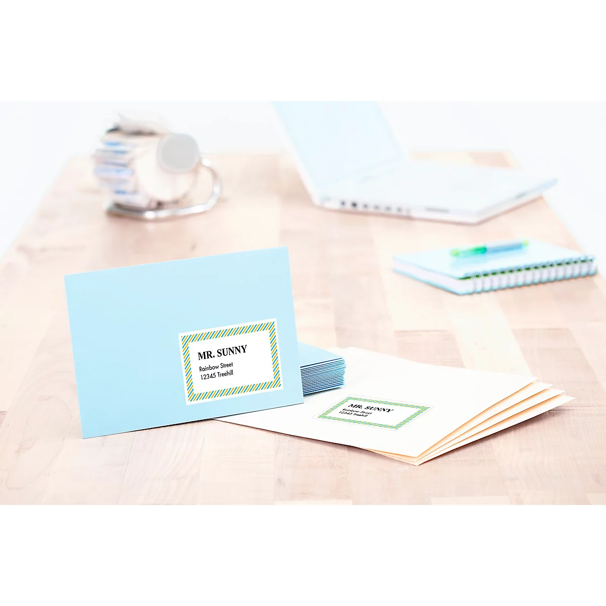 Lichtblauwe envelop met adressticker "Mr. Sunny" op houten tafel. Op de achtergrond: laptop en notitieboek.