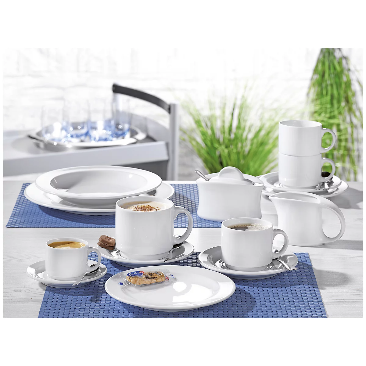 Coffee set with cups, saucers, milk jug and sugar bowl on a table. Plants can be seen in the background.