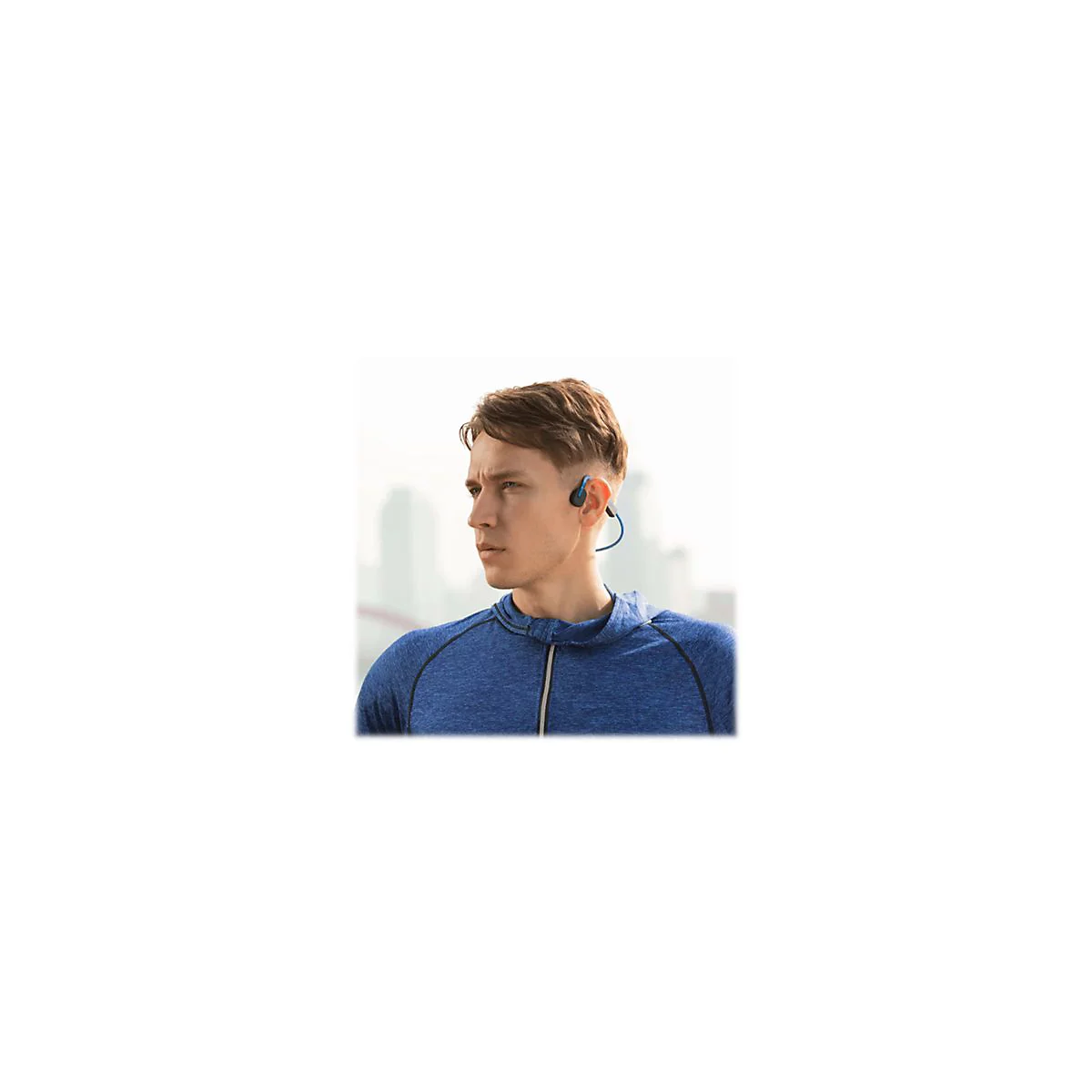 Junger Mann mit Bone Conduction KopfhÃ¶rern. Er trÃ¤gt ein blaues Sweatshirt und schaut zur Seite.