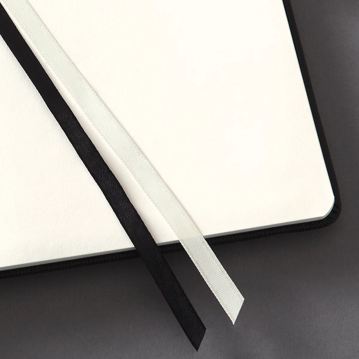 Gros plan d'un carnet ouvert avec des signets en ruban noir et blanc sur des pages claires. Fond gris.
