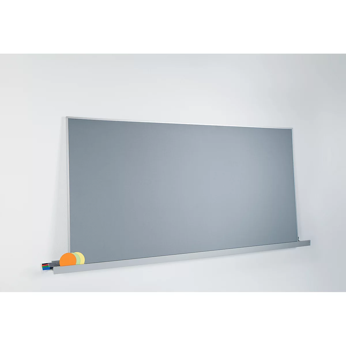 Graue Tafel mit Stiften und Schwämmen an weißer Wand.