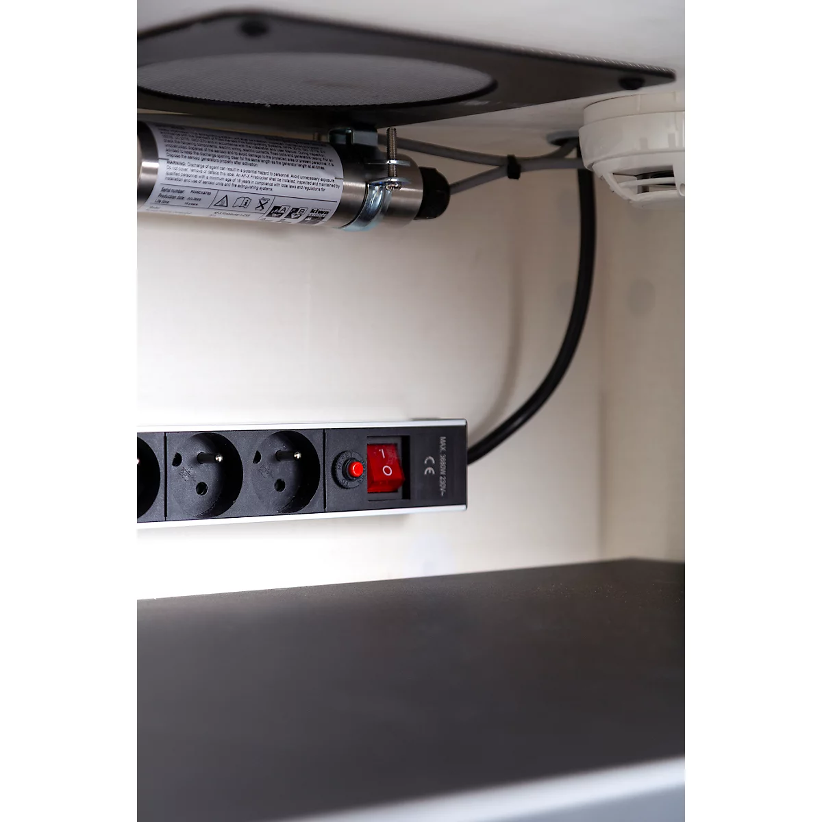 Detailaufnahme einer Steckdosenleiste mit rotem Schalter. Darüber ein Rauchmelder und eine Metallröhre.
