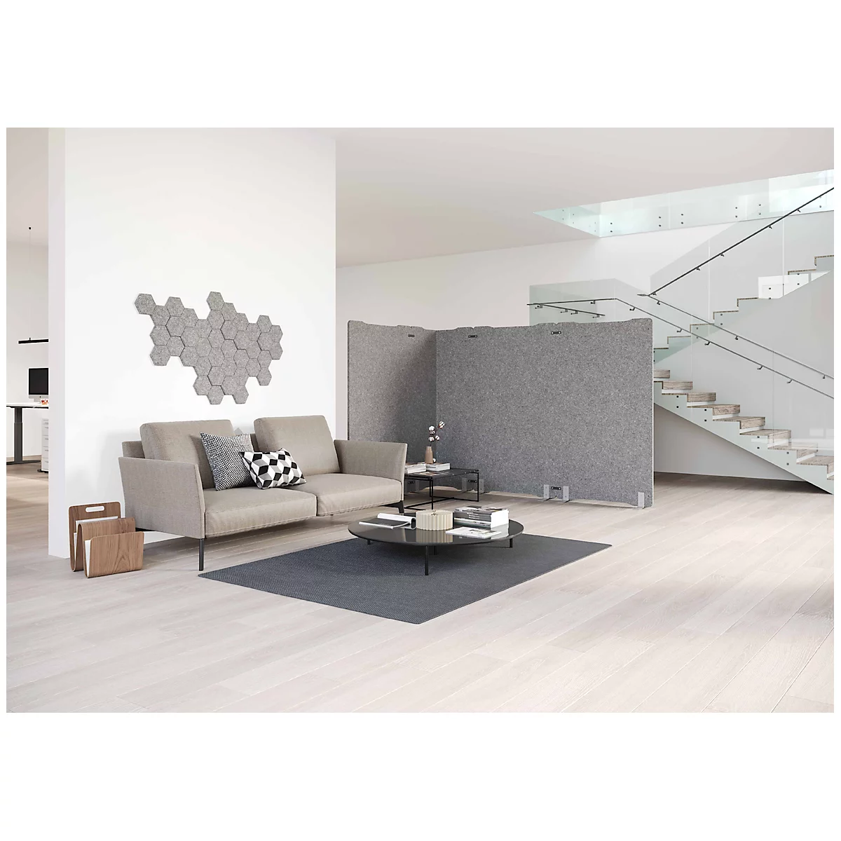 Een lichte woonkamer met een bank, salontafel, room dividers en trap. Zeshoekige grijze elementen zijn aan de muur bevestigd.