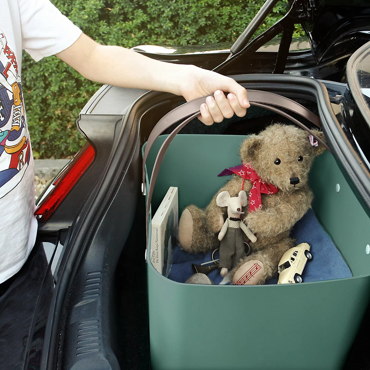 Person lifting a basket full of toys out of the trunk of a car.