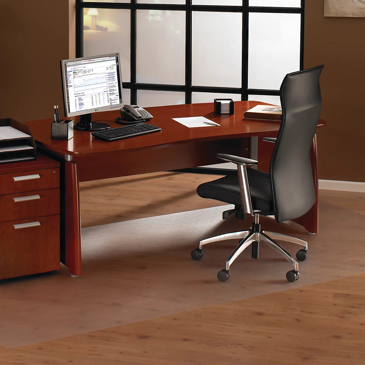 Oficina con escritorio, silla y PC. Una alfombra transparente está sobre el suelo de madera.