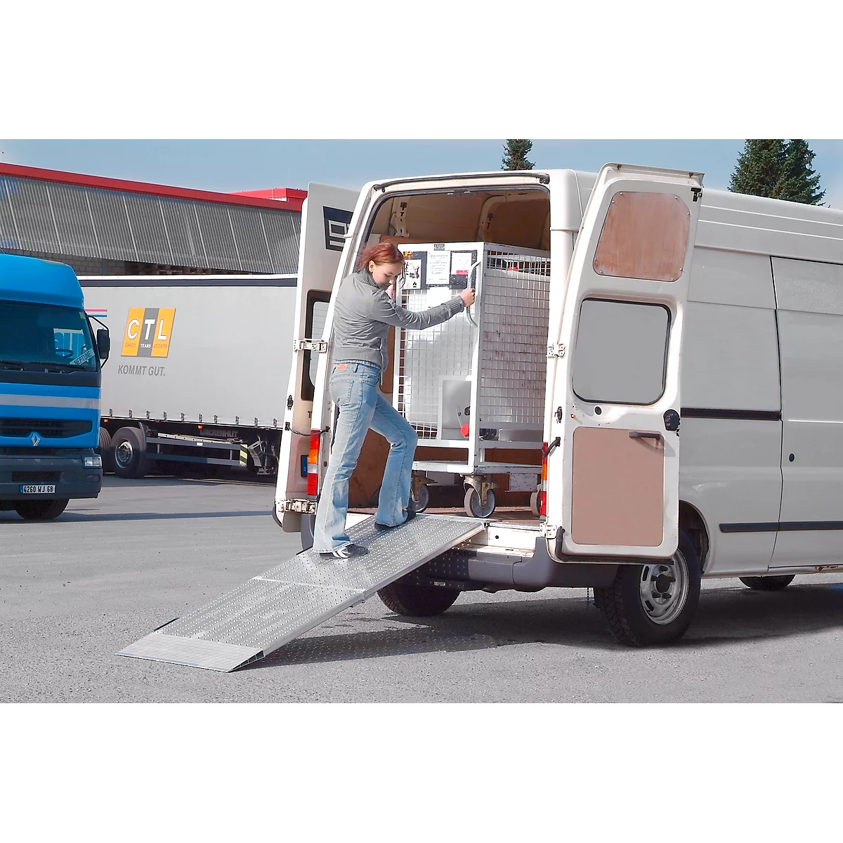 A woman is loading a white van with a metal cage. A loading ramp is unfolded.