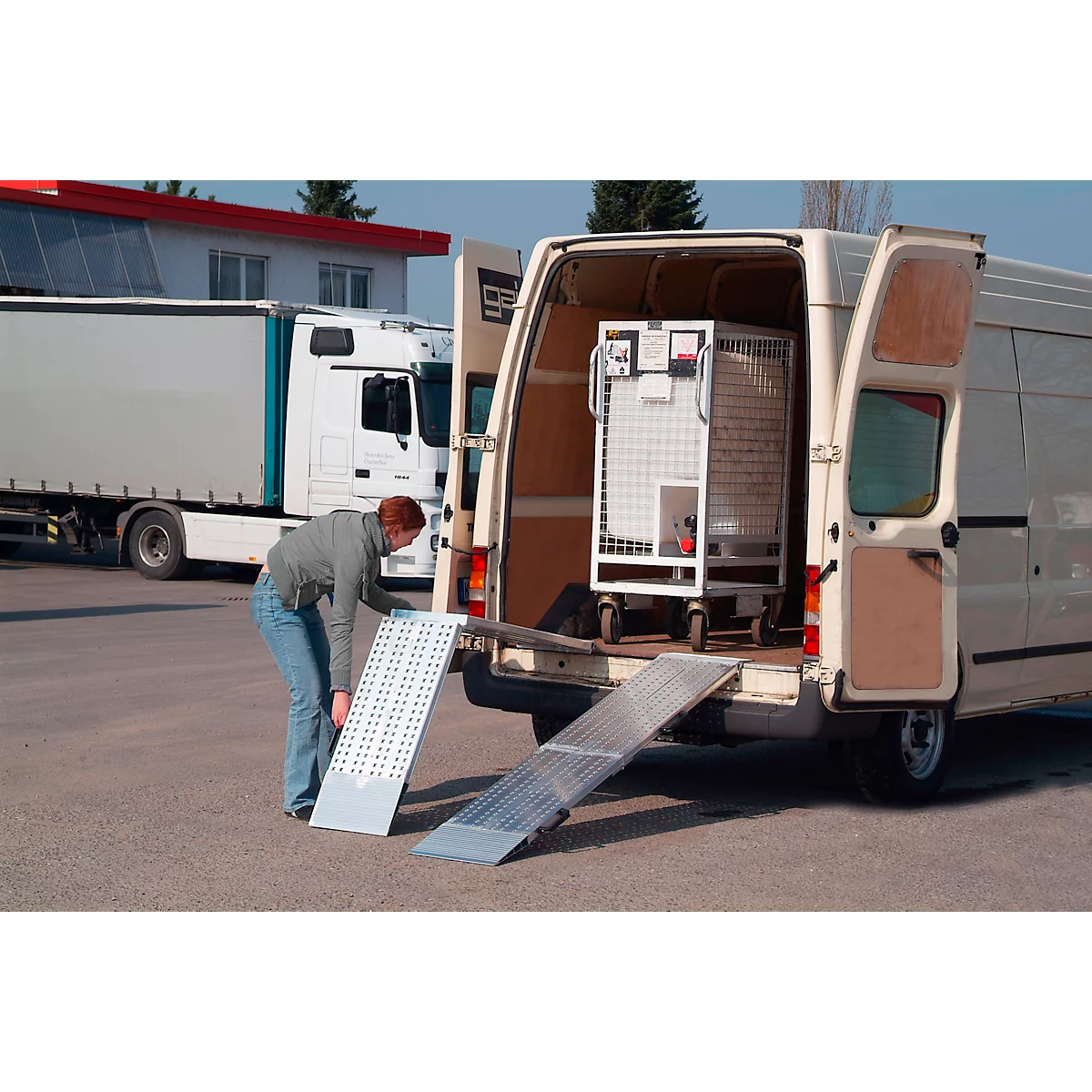 A man sets up a ramp on a white van. There is a metal cage in the van.
