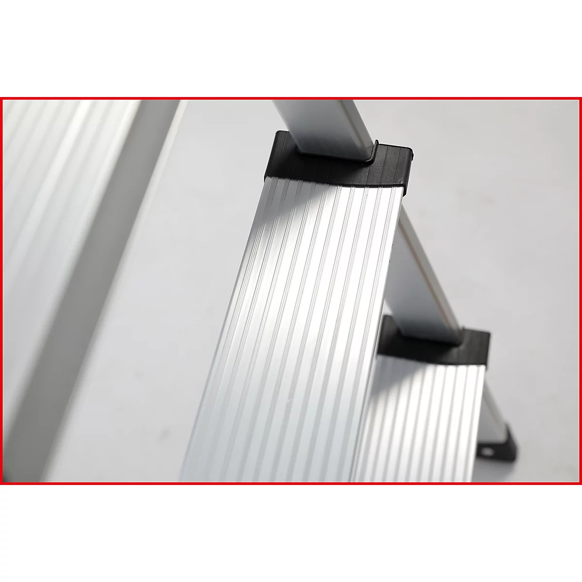Nahaufnahme einer Aluminiumleiter mit schwarzen Kunststofffüßen auf weißem Hintergrund. Die Sprossen sind geriffelt.