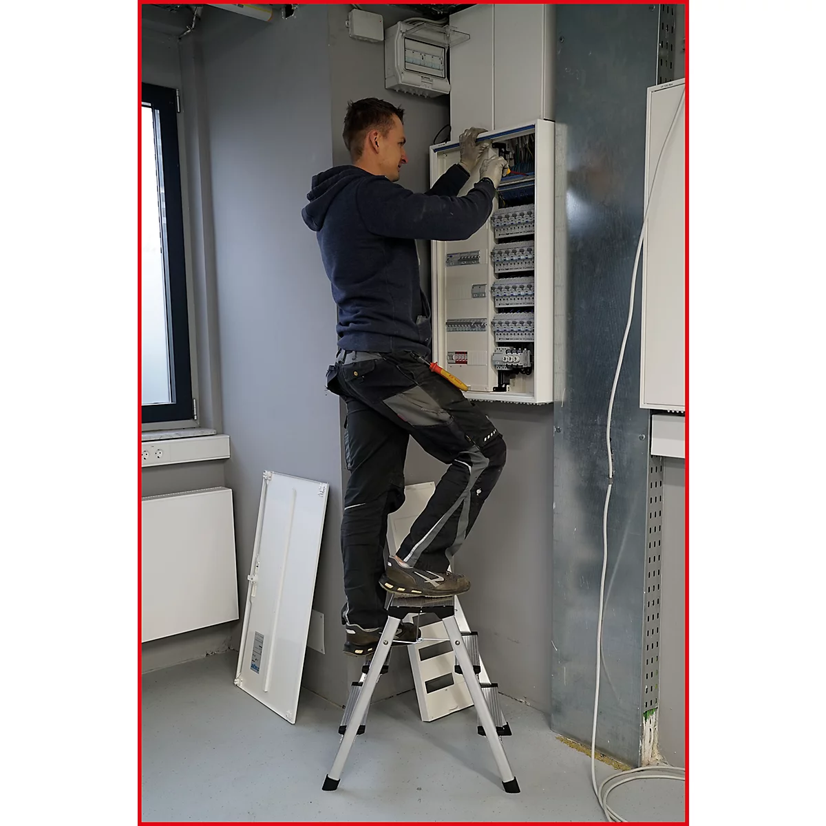 Ein Elektriker arbeitet an einem Sicherungskasten, er steht auf einer Trittleiter.