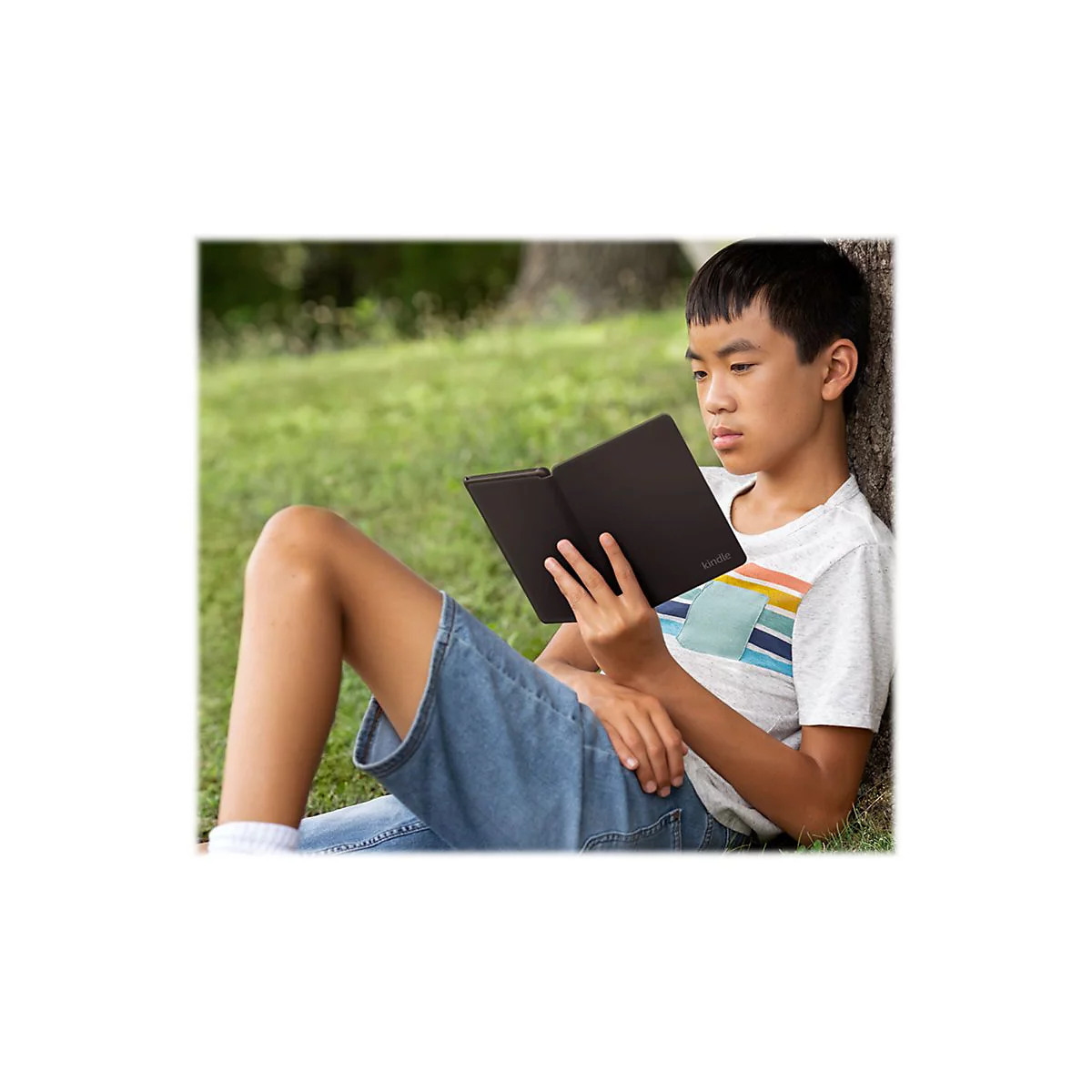 Ein Junge sitzt im Gras, lehnt an einem Baum und liest ein schwarzes E-Book.