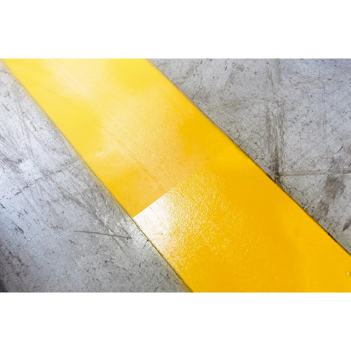 Yellow paint stripe on grey concrete. The paint is glossy and covers the concrete unevenly.