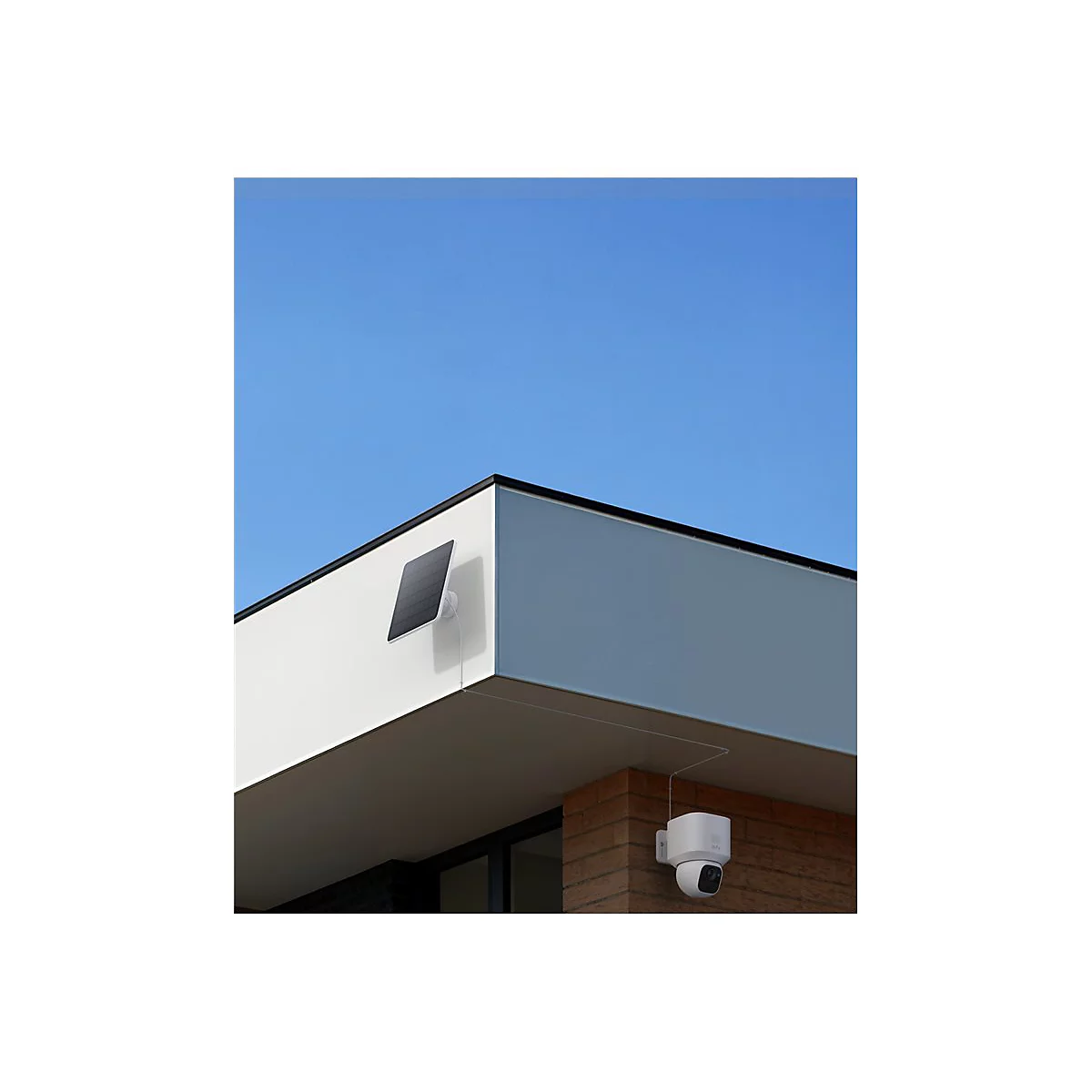 Überwachungskamera und Solarpanel an einer Hauswand vor blauem Himmel.