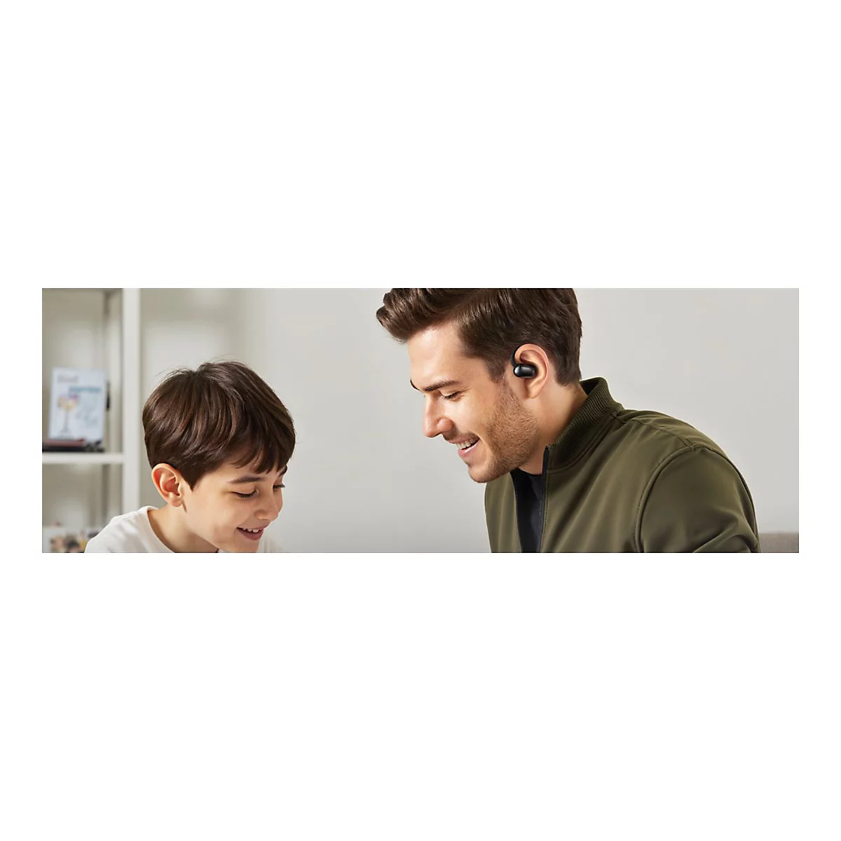 Ein lächelnder Vater trägt einen schwarzen In-Ear-Kopfhörer und schaut liebevoll auf seinen lachenden Sohn.