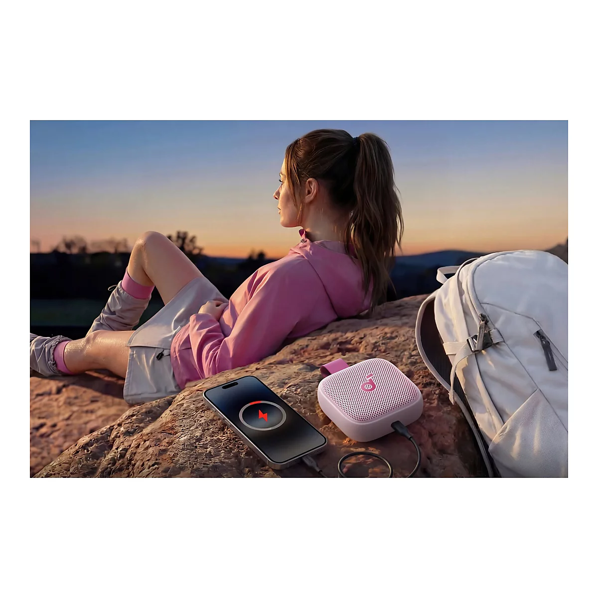 Frau entspannt sich in der Natur, während ihr Smartphone an einem pinken Soundcore-Lautsprecher lädt.