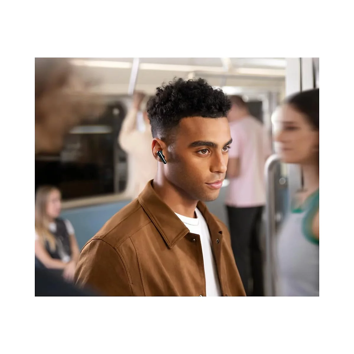 Ein Mann mit Kopfhörern in einer U-Bahn. Er trägt eine braune Jacke und blickt nach rechts. Mehrere andere Personen sind unscharf im Hintergrund zu sehen.