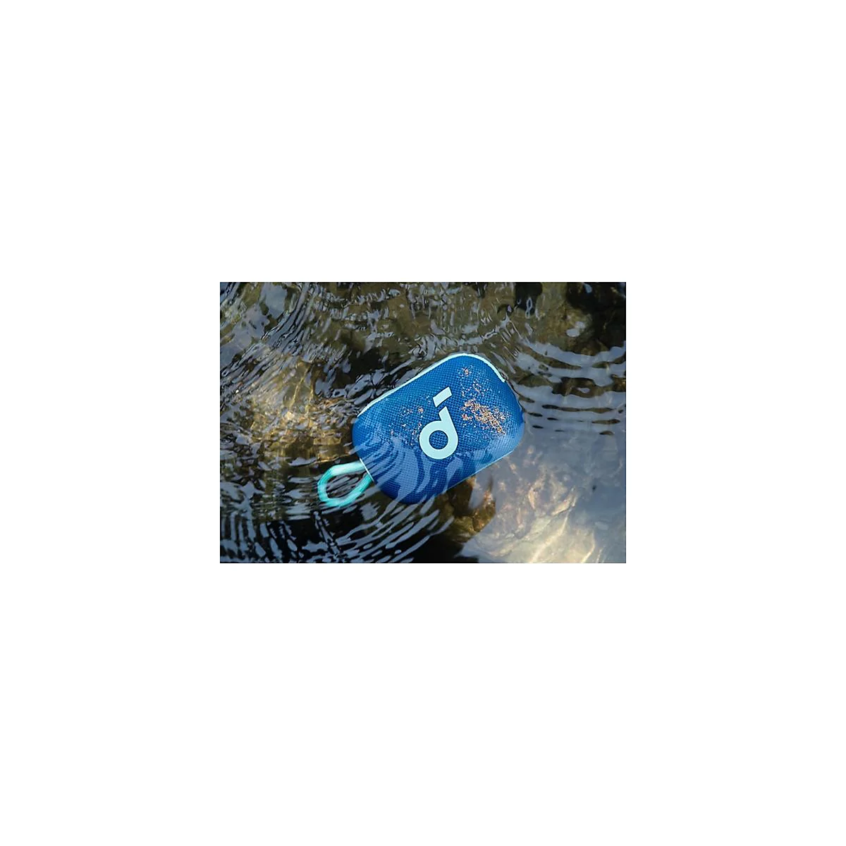 Ein blauer, wasserfester Lautsprecher mit Trageschlaufe schwimmt halb untergetaucht in einem fließenden Bach.