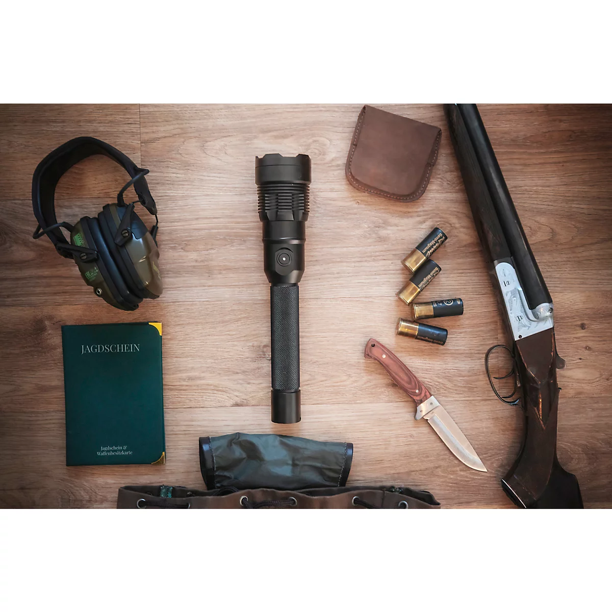 Hunting gear on wood: rifle, ammunition, knife, flashlight, hearing protection, notebook.