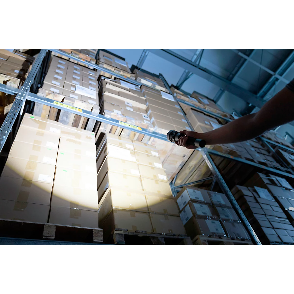 A person is shining a flashlight in a warehouse shelf with boxes. The angle is low.