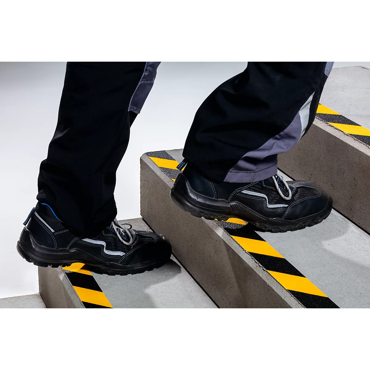 Person stepping up stairs, black shoes, yellow and black warning stripes on steps.