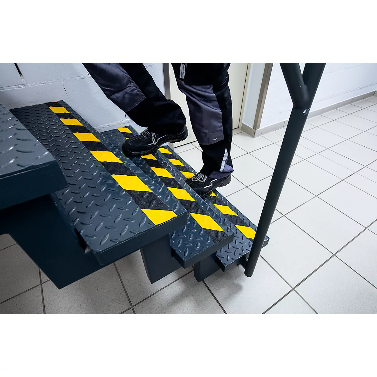 Person climbing stairs with yellow and black markings. Metal railing.