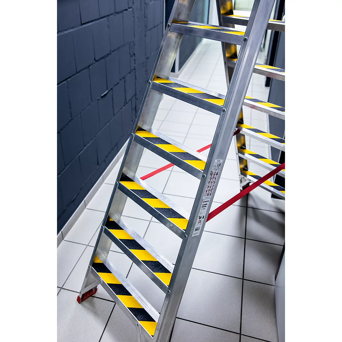 Aluminum ladder with black and yellow stripes on the steps, standing in a room with a dark wall.