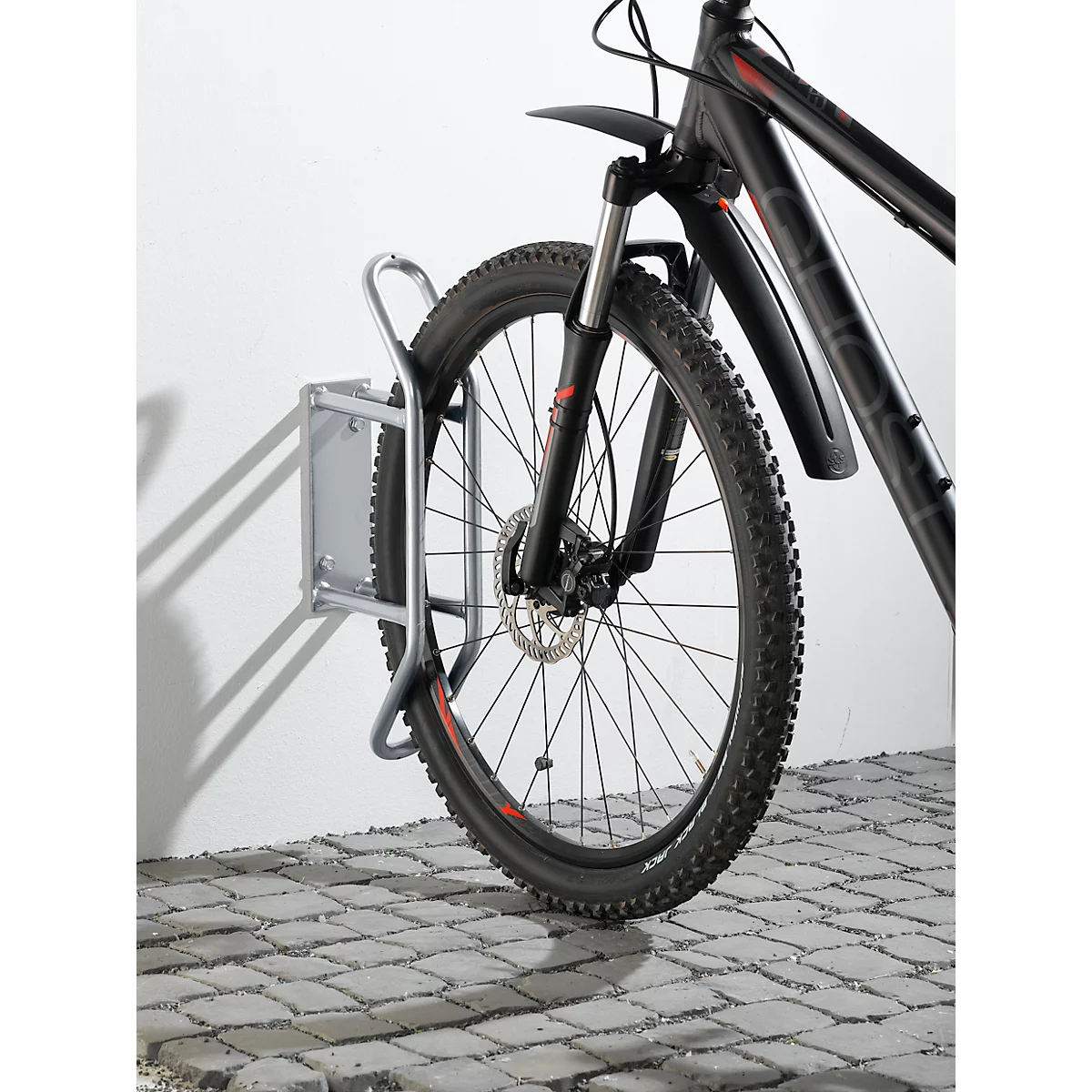 Una bicicleta de montaña negra en un soporte de pared. La rueda delantera de la bicicleta es visible.