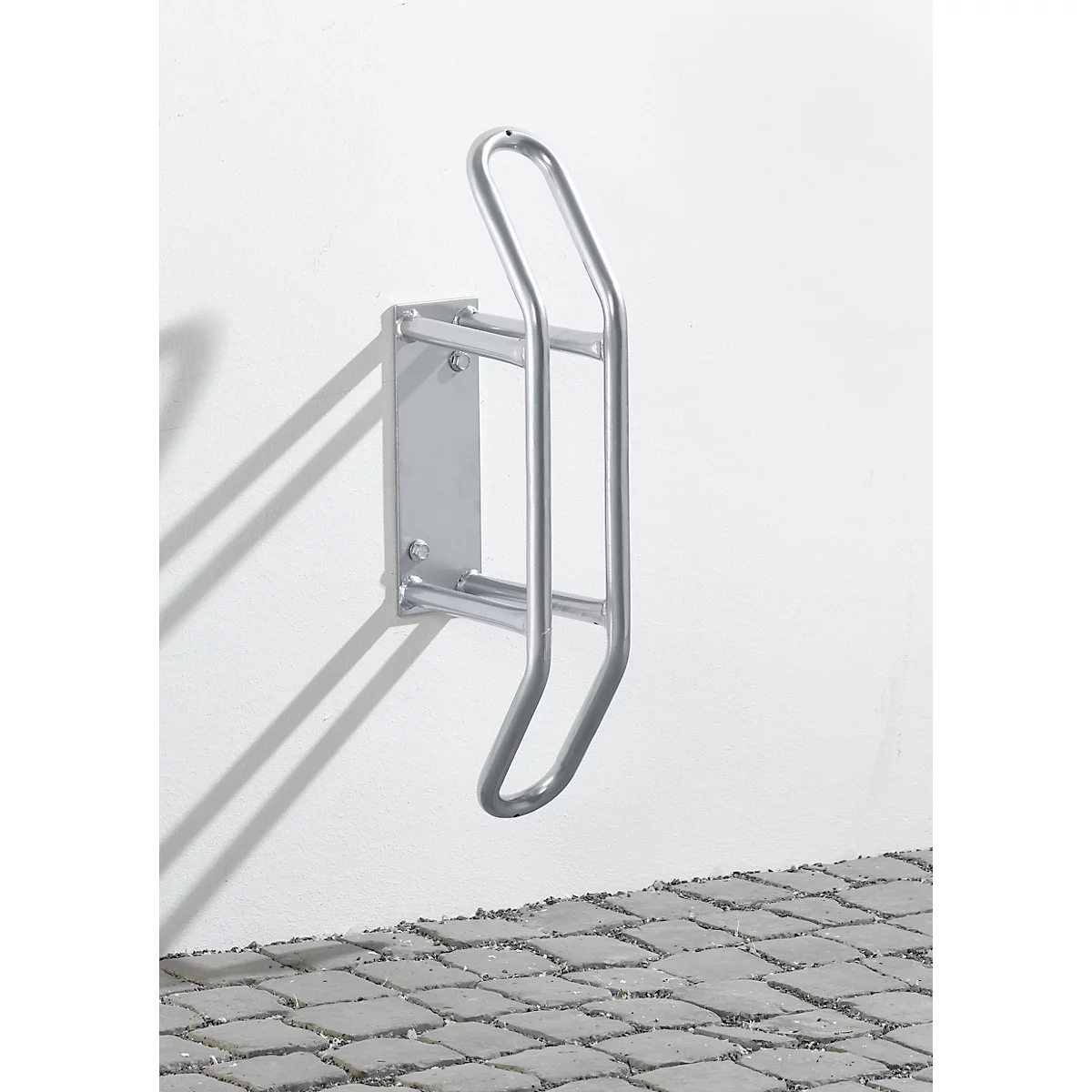 Soporte de bicicleta metálico en una pared blanca, adoquines debajo.