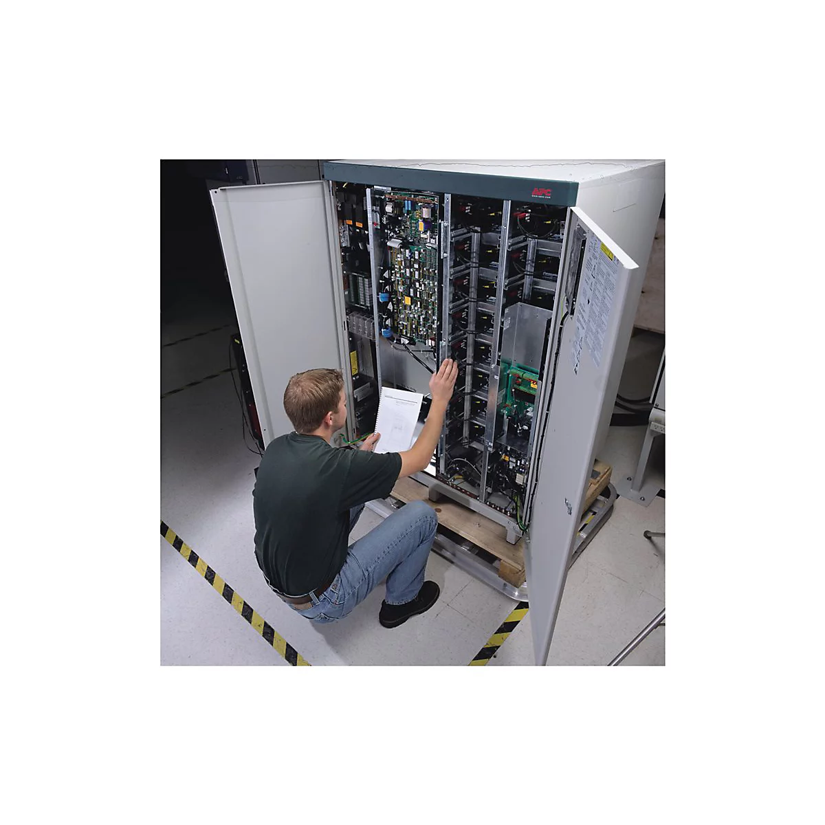 Ein Mann sitzt vor einem geöffneten Server-Rack, das er wartet. Er hat ein Blatt Papier in der Hand.