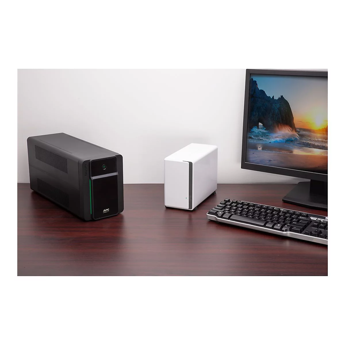 Schwarze USV und weiße Festplatte stehen auf einem Schreibtisch neben Monitor und Tastatur.