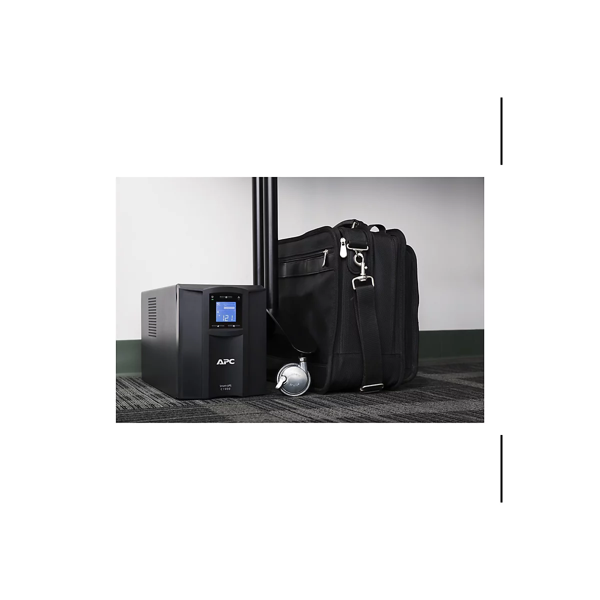 Ein schwarzes APC Smart-UPS C1000 steht neben einer schwarzen Aktentasche und einem Stuhl. Auf dem UPS-Display werden Zahlen angezeigt.