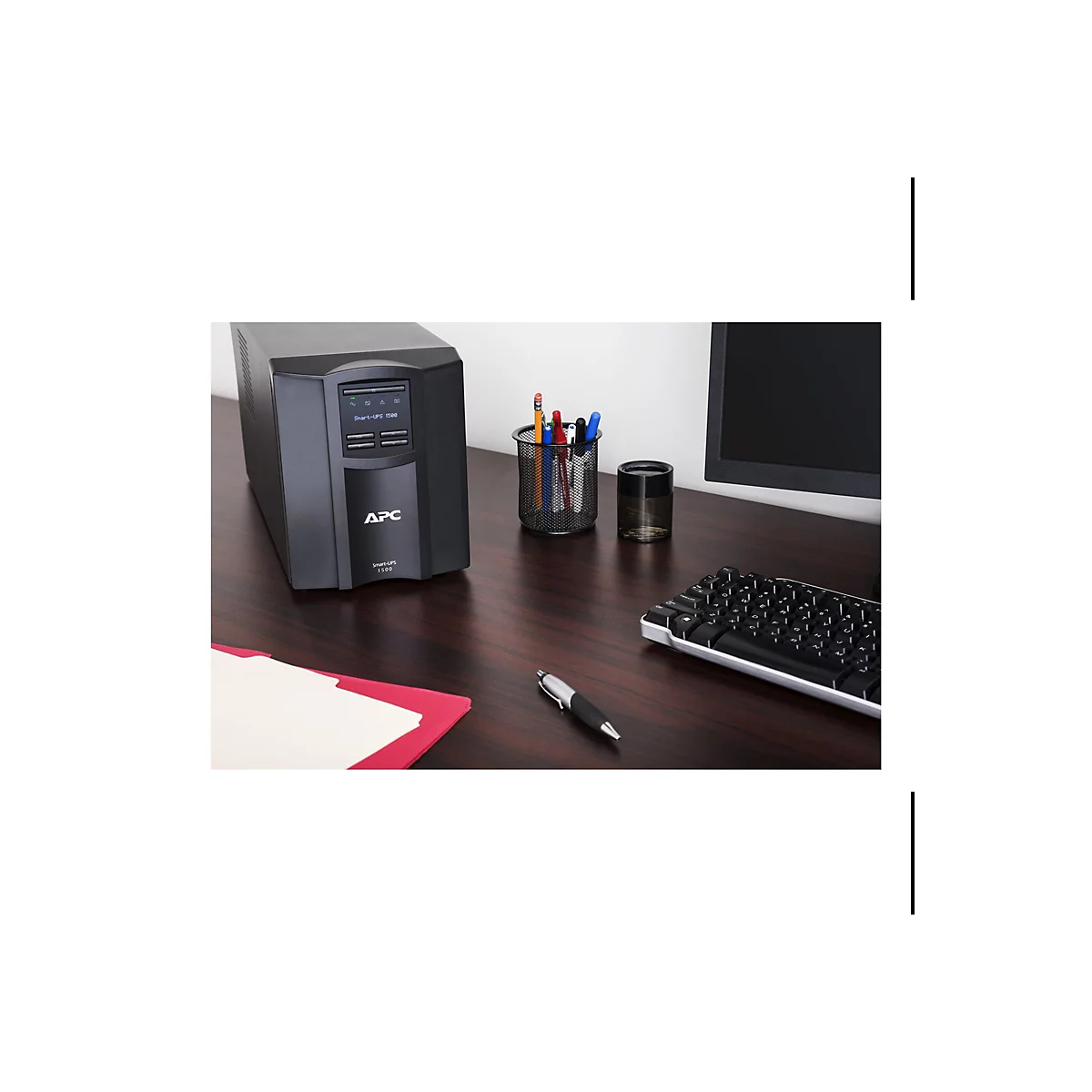 Un onduleur APC noir est posé sur un bureau marron. À côté, un moniteur, un porte-stylo, un clavier et un stylo.