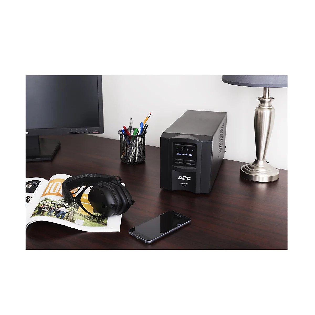 Ein schwarzes APC-USV-GerÃ¤t steht auf einem Schreibtisch neben einem Monitor, KopfhÃ¶rern und einem Smartphone.
