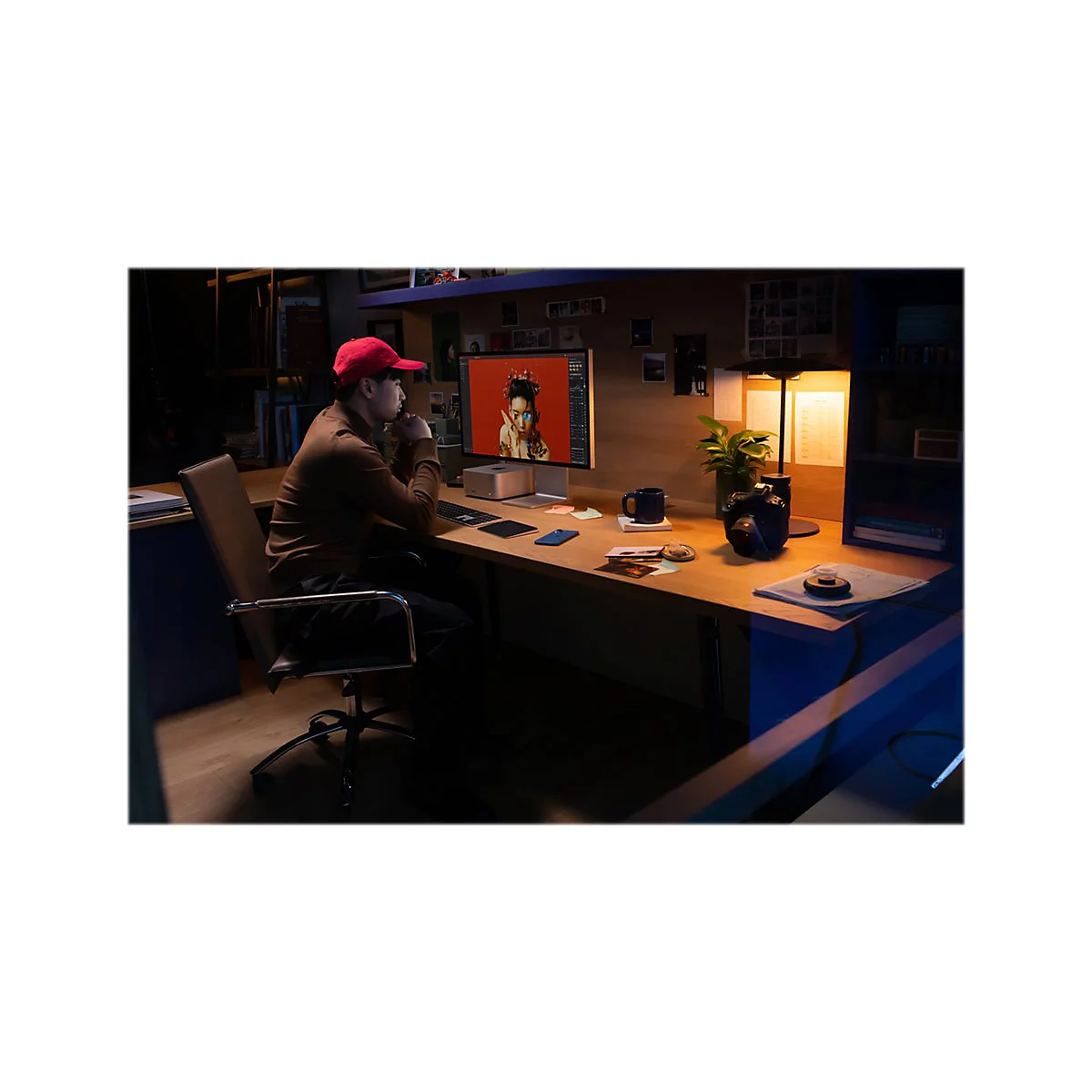 Ein Mann mit roter Kappe sitzt an einem Schreibtisch und arbeitet am Computer. Der Bildschirm zeigt eine Person, die ein rotes Oberteil trÃ¤gt.