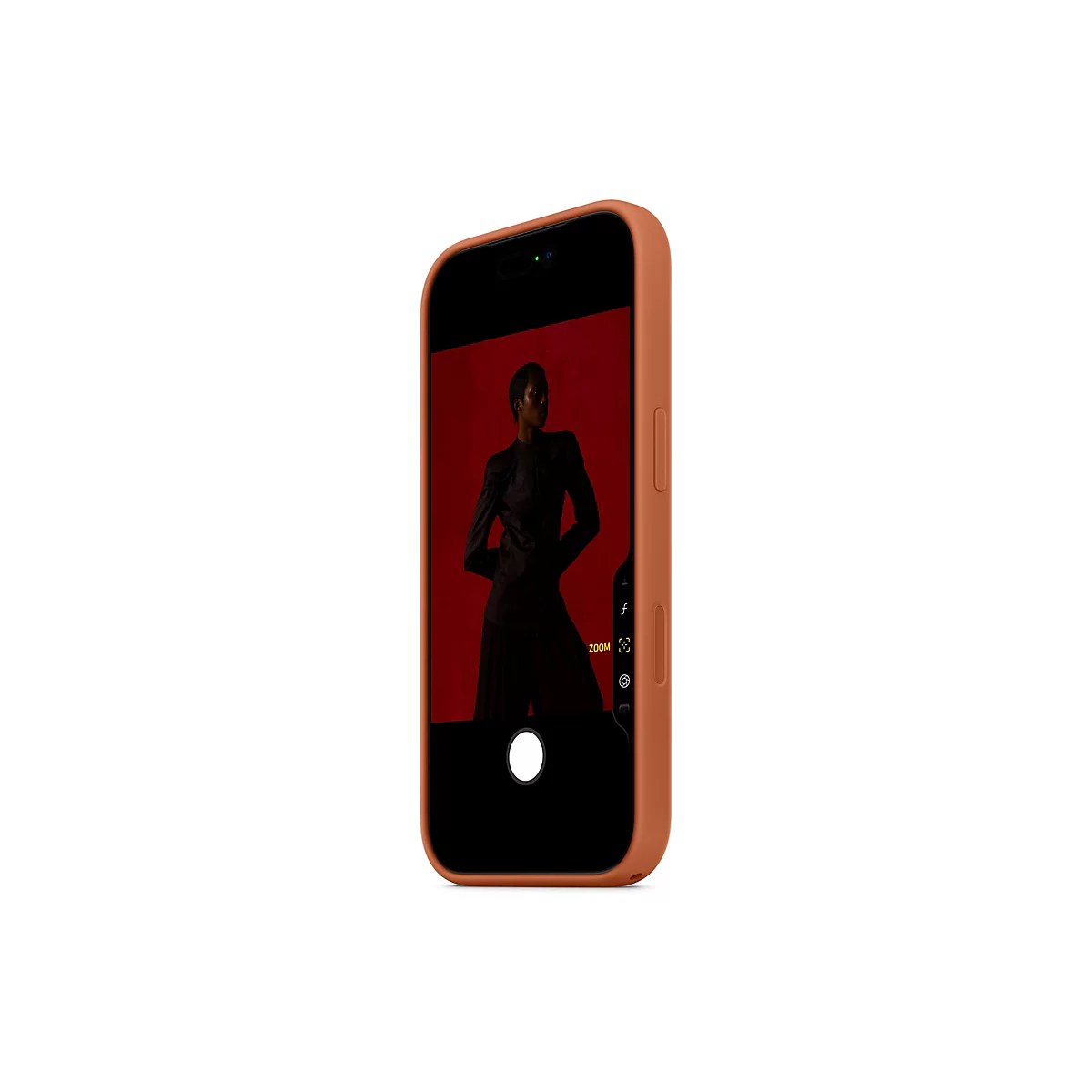 Ein Handy mit einer orangefarbenen Hülle zeigt ein Foto einer Person mit schwarzer Kleidung vor rotem Hintergrund. Auf dem Bildschirm sind Kamera-Icons zu sehen.